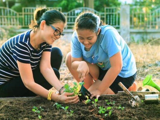 two teenage girls planting vegetables in a community garden